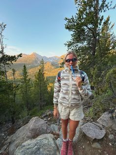 a woman standing on top of a mountain holding a blue toothbrush in her mouth