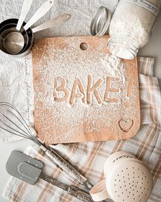 baking utensils and flour on a towel with the word bake spelled in powdered sugar