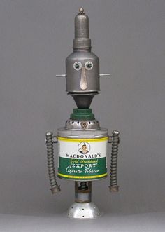 a robot made out of tin cans sitting on top of a white table next to a gray wall