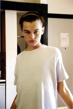 a young man standing in front of a mirror with his hand on his hip while wearing a white t - shirt