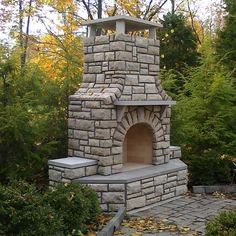 an outdoor brick oven in the middle of some bushes and trees with yellow leaves around it