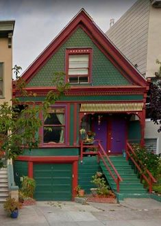 a green and red house with stairs leading up to the front door, on a street corner