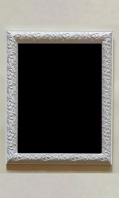 an ornate white frame hanging on the wall with a black square in front of it