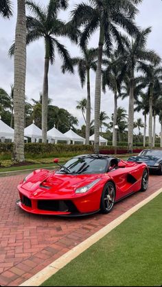 two red sports cars parked next to each other on a brick road near palm trees