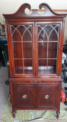 a wooden china cabinet with glass doors on the front and side panels, sitting on top of a checkered table cloth