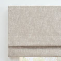 a beige roman blind in front of a window with the blinds pulled back to reveal an off - white background