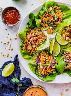 a white plate topped with lettuce salad next to two bowls of sauces