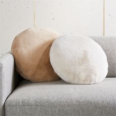 two round pillows sitting on top of a gray couch next to a white and brown pillow