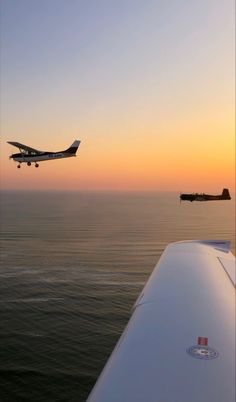 an airplane flying over the ocean with another plane in the sky above it at sunset