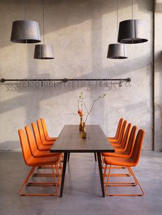 an orange table with six chairs and a vase filled with flowers on the top, in front of two hanging lamps