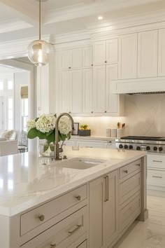 a large kitchen with white cabinets and marble counter tops is pictured in this image, there are flowers on the island