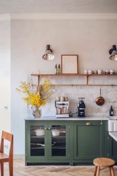 a kitchen with green cabinets and white tile backsplash, yellow flowers in a vase on the counter