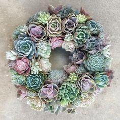 a wreath made out of succulents sits on the ground in front of a wall