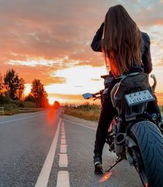 a woman riding on the back of a motorcycle down a road at sunset or sunrise