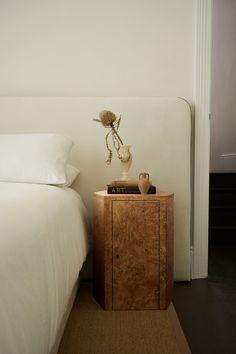 a white bed sitting next to a nightstand with a vase on it's side