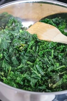 spinach being cooked in a pot with a wooden spoon