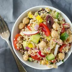 a white bowl filled with rice, vegetables and chickpeas next to a fork