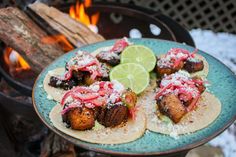 three tacos on a blue plate with lime wedges and red onion garnish