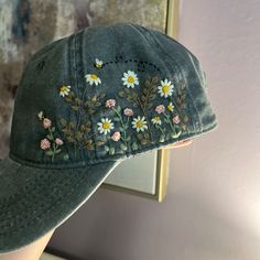 a woman's hat with daisies and bees embroidered on the side, in front of a mirror