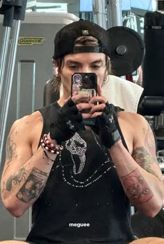 a man with tattoos taking a selfie in front of a gym machine while holding a cell phone