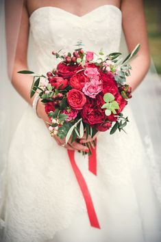 a bride holding a bouquet of red flowers