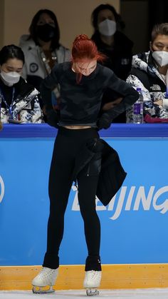 a woman with red hair standing on the ice in front of an audience wearing face masks