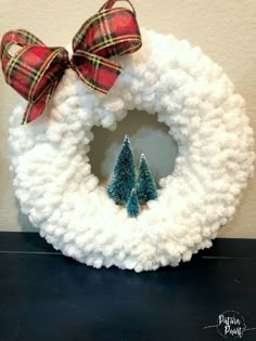 a knitted wreath with two small trees on it and a bow hanging from the front