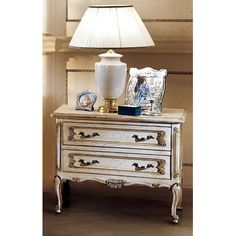 a white lamp sitting on top of a table next to a chest of drawers with pictures