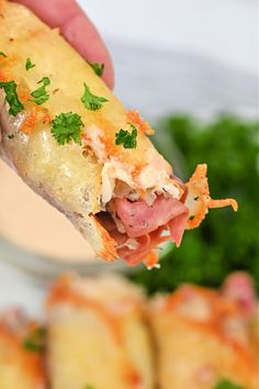 a hand holding up a piece of food with meat and cheese on it next to some vegetables