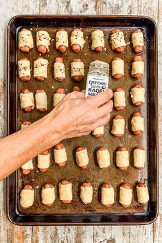 a person holding a jar of hotdogs in front of a tray of pigs in a blanket