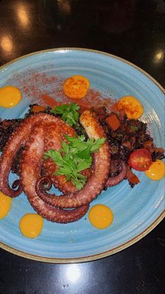 an octopus is on a blue plate with yellow sauces and garnishes