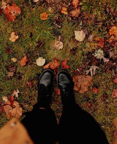 a person standing in the grass with their feet up and wearing black shoes, looking down