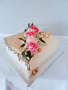 a white cake with pink flowers and gold numbers on it's side, sitting on a clear platter