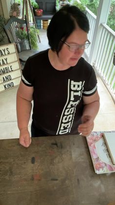 a woman standing at a wooden table with a book in front of her and looking down