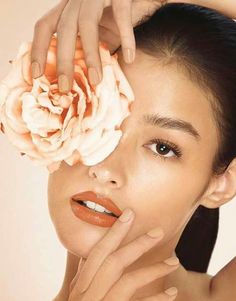 a woman holding a flower in front of her face and touching it with her hands