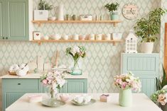 a kitchen with green cabinets and white counter tops next to shelves filled with potted plants