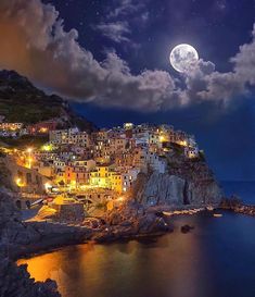 the moon is shining over an island with houses on it and water below, under a cloudy night sky