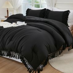 a black comforter with tassels on it in a white room next to a window