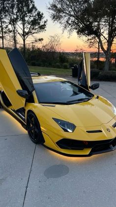 a yellow sports car parked on the side of a road with its doors open at sunset