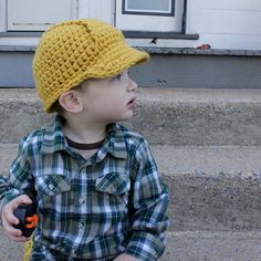 a young boy sitting on the steps wearing a yellow knitted hat and holding a measuring tape