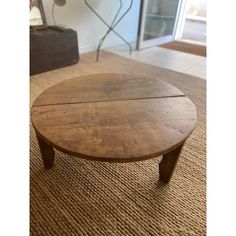 a round wooden table sitting on top of a carpeted floor next to a window