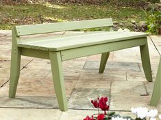 a green bench sitting on top of a stone floor next to flowers and trees in the background