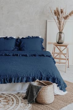 a bed with blue sheets and pillows in a room next to a basket on the floor