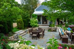 an outdoor dining area in the middle of a garden with lots of flowers and greenery