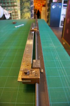 a close up of a long piece of metal on a green cutting mat with two people in the background