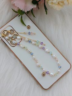 a cell phone case with pearls and charms on it next to some flowers in a vase