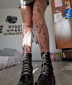 the legs and ankles of a woman with tattoos on her body, wearing black boots