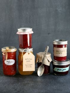 jam jars with labels and spoons are lined up against a gray background for display