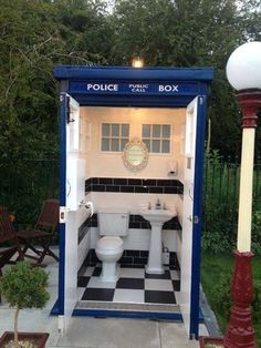 a small bathroom with a toilet and sink in the middle of a garden area next to a lamp post