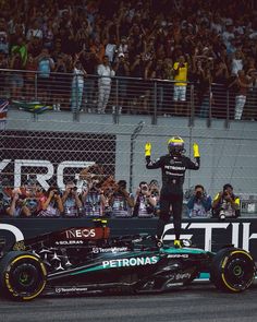 a man standing on the back of a racing car in front of a large crowd